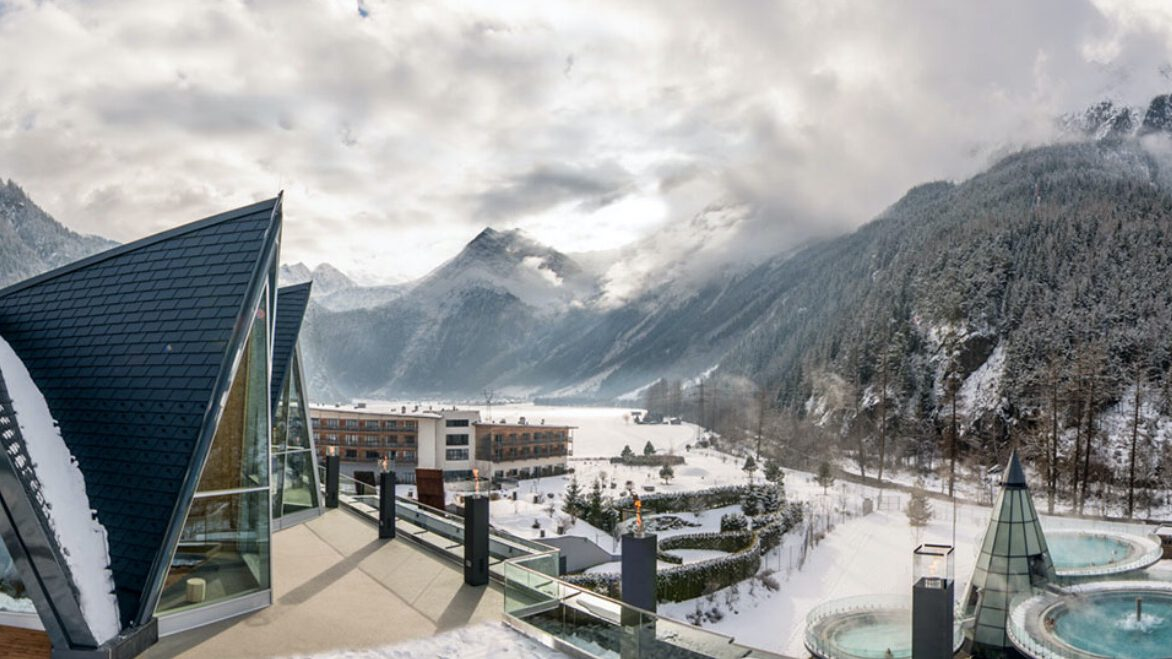 Dieses moderne Gebäude erinnert an eine Galerie und besticht durch seine dreieckigen Dächer mit Blick auf eine schneebedeckte Berglandschaft. Genießen Sie die ruhige Aussicht vom Außenpool unter bewölktem Himmel.