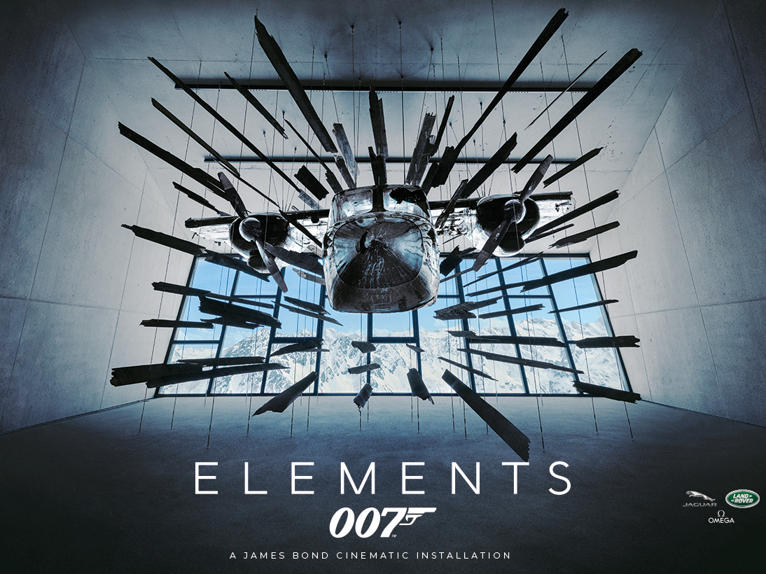 Un'installazione di un aereo è sospesa a mezz'aria con pezzi frammentati che si irradiano verso l'esterno. La parola "Elements" e il logo di 007 sono visualizzati sotto.