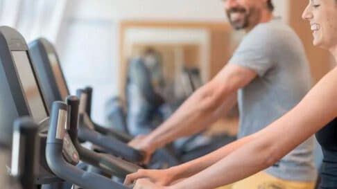 Zwei lächelnde Menschen, die in einem Fitnessstudio Trainingsgeräte benutzen.