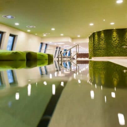 Modernes Interieur mit grünen Akzenten, reflektierendem Boden, geschwungener Wand mit Laub, Einbauleuchten und großen Fenstern.