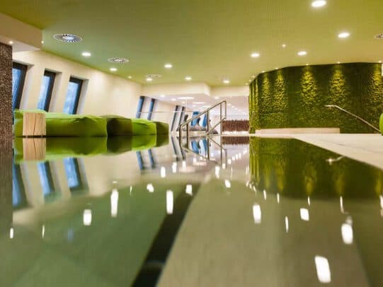 Modernes Interieur mit grün-weißem Dekor, reflektierendem Boden, grünen Sofas, Wandverkleidungen und Decke. Helle Beleuchtung und eckige Fenster sorgen für ein elegantes Ambiente.