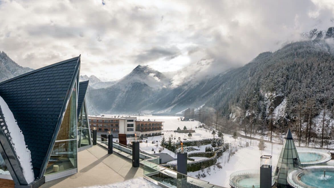 Dieses moderne Gebäude erinnert an eine Galerie und besticht durch seine dreieckigen Dächer mit Blick auf eine schneebedeckte Berglandschaft. Genießen Sie die ruhige Aussicht vom Außenpool unter bewölktem Himmel.