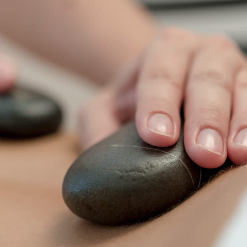 Close-up of hands placing smooth black stones on a persons back during a soothing session at the thermal spa.