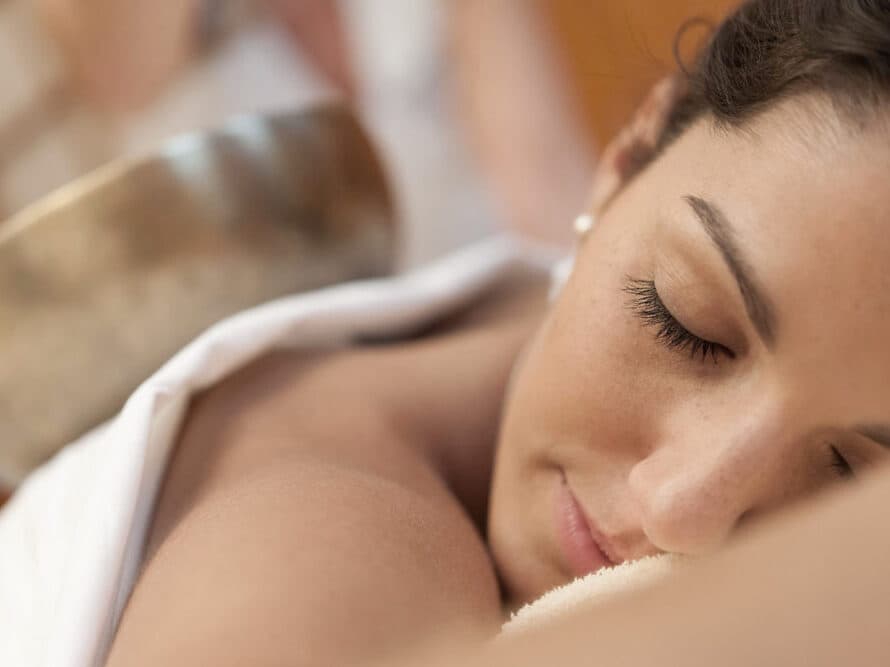 Person receiving a relaxing massage, eyes closed, draped with a white towel on a massage table, with a blurred background.