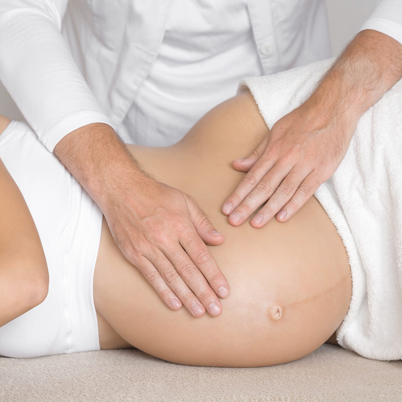 Person, die von einem Fachmann eine Bauchmassage erhält, wobei die Hände sanften Druck auf den Bauchbereich ausüben.