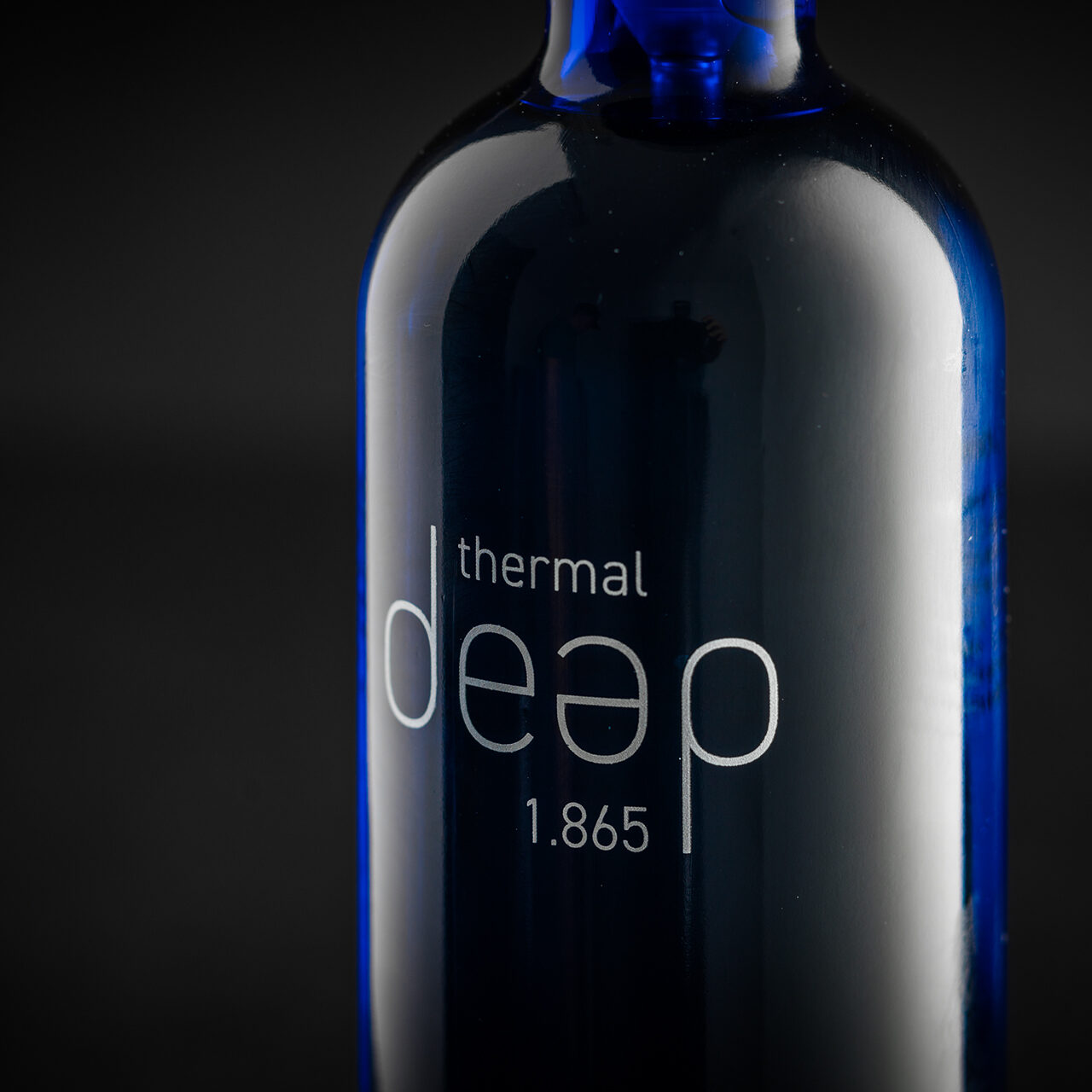 Primo piano di una bottiglia di vetro blu con l'etichetta "thermal deap 1.865" su uno sfondo scuro.