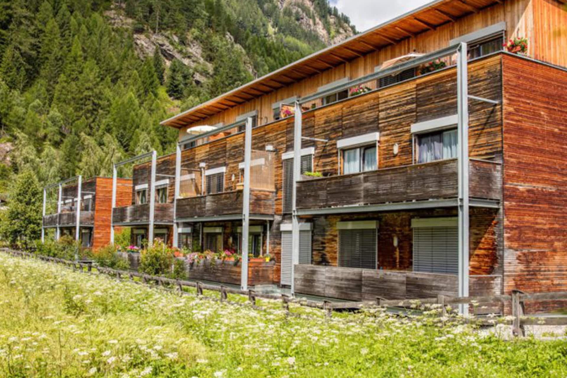 Ein modernes Apartmentgebäude aus Holz mit Balkonen, umgeben von üppigem Grün und Bäumen in einer bergigen Gegend.