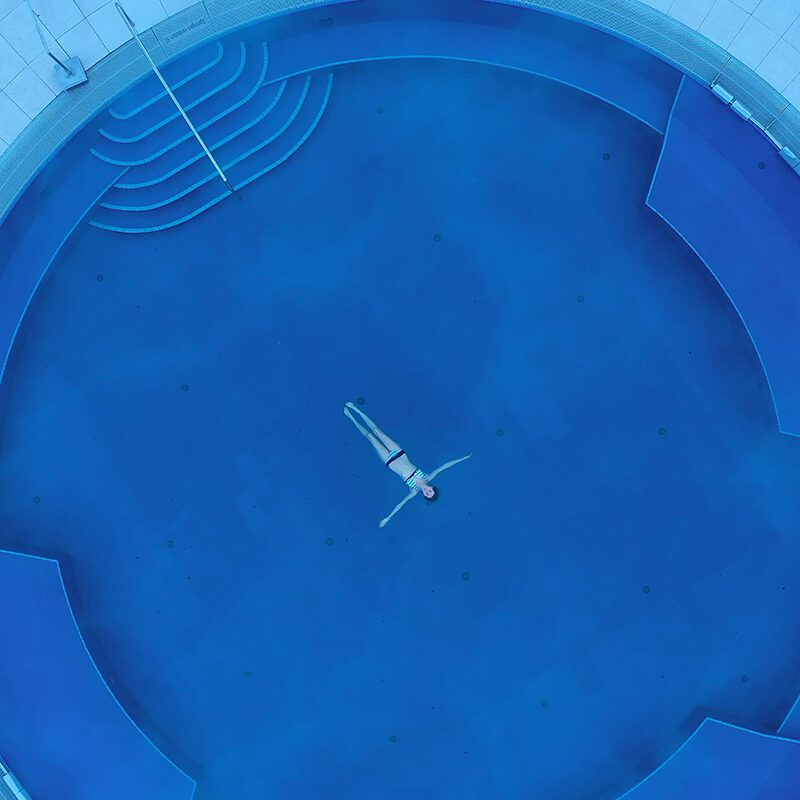 Person, die auf dem Rücken in einem großen, runden blauen Schwimmbecken mit gefliesten Rändern und Stufen schwimmt.