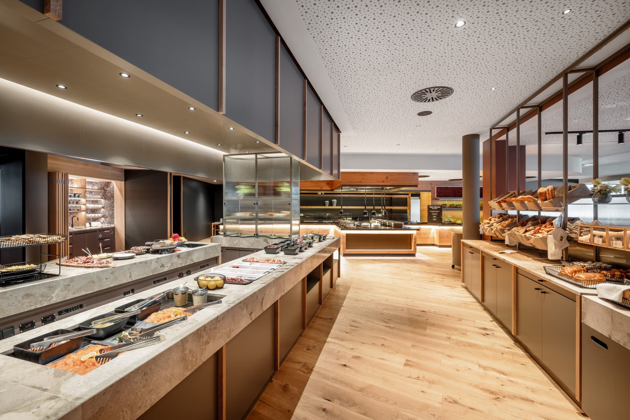 In un ambiente ispirato ai ristoranti, questo buffet moderno presenta ripiani eleganti e pavimenti in legno. L'illuminazione brillante mette in risalto la serie organizzata di postazioni di cibo, che mettono in mostra una squisita selezione di piatti e pani.