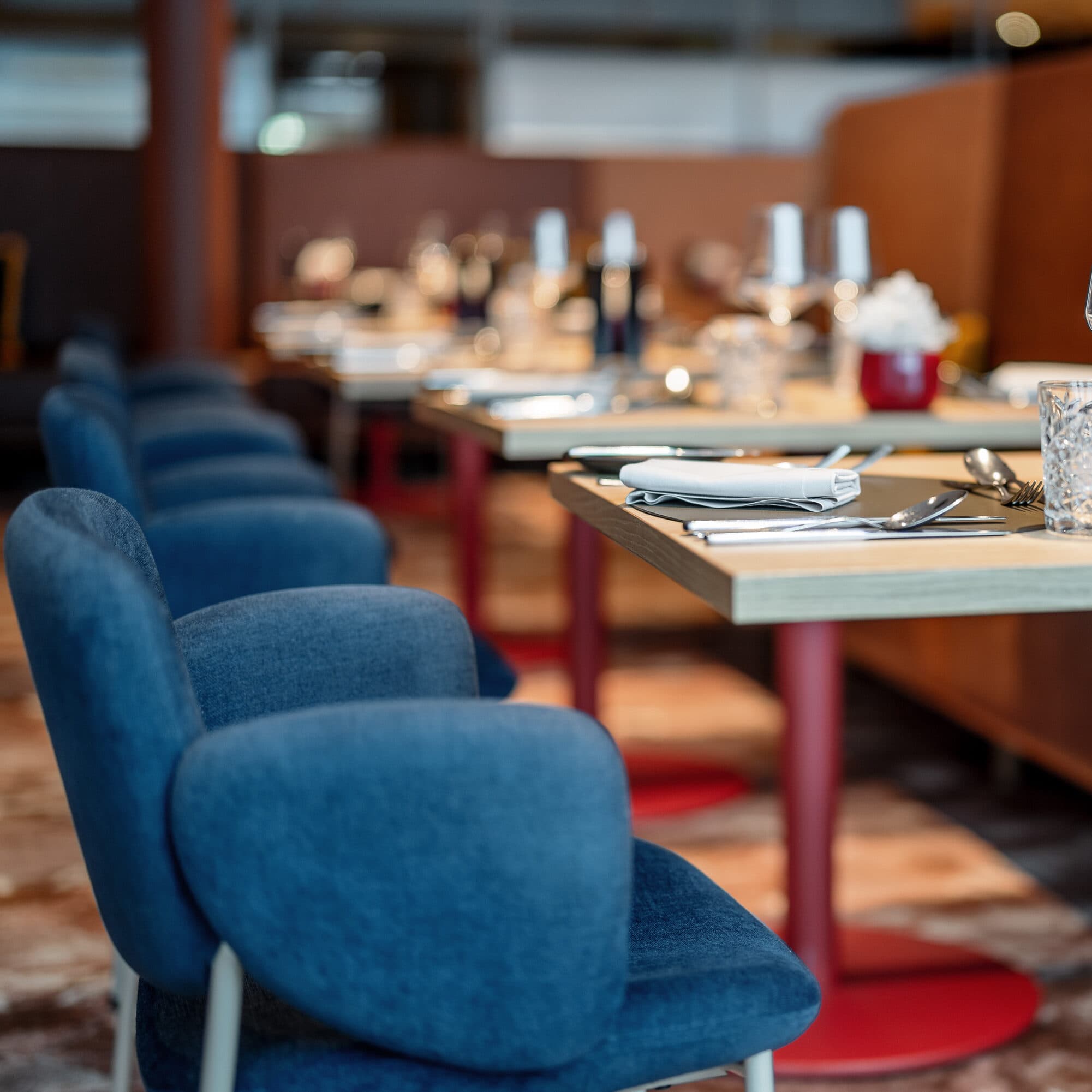 Un ristorante in stile ristoranti, con sedie imbottite blu e tavoli apparecchiati con cura, con bicchieri da vino e posate, su un pavimento in moquette a motivi.