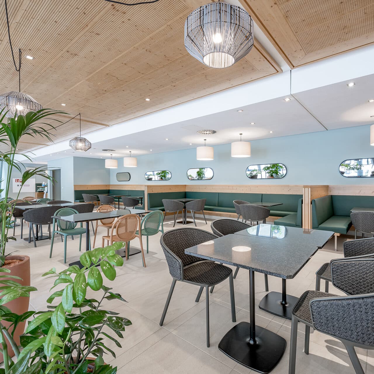 Ce café moderne, orné de plantes, de chaises en osier et d'une décoration en bois, offre un véritable havre de paix culinaire. Les tables sont dressées sous des suspensions lumineuses, et des banquettes vert menthe, le long du mur, sont surmontées de miroirs. Le plafond, orné de panneaux de bois, complète ce havre de paix thermal.