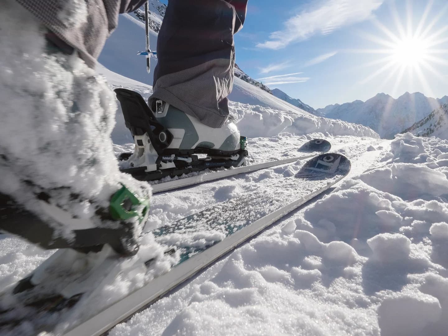 Close-up view of a person skiing on snowy terrain during a winter holiday, with sunlight shining over mountains in the background.