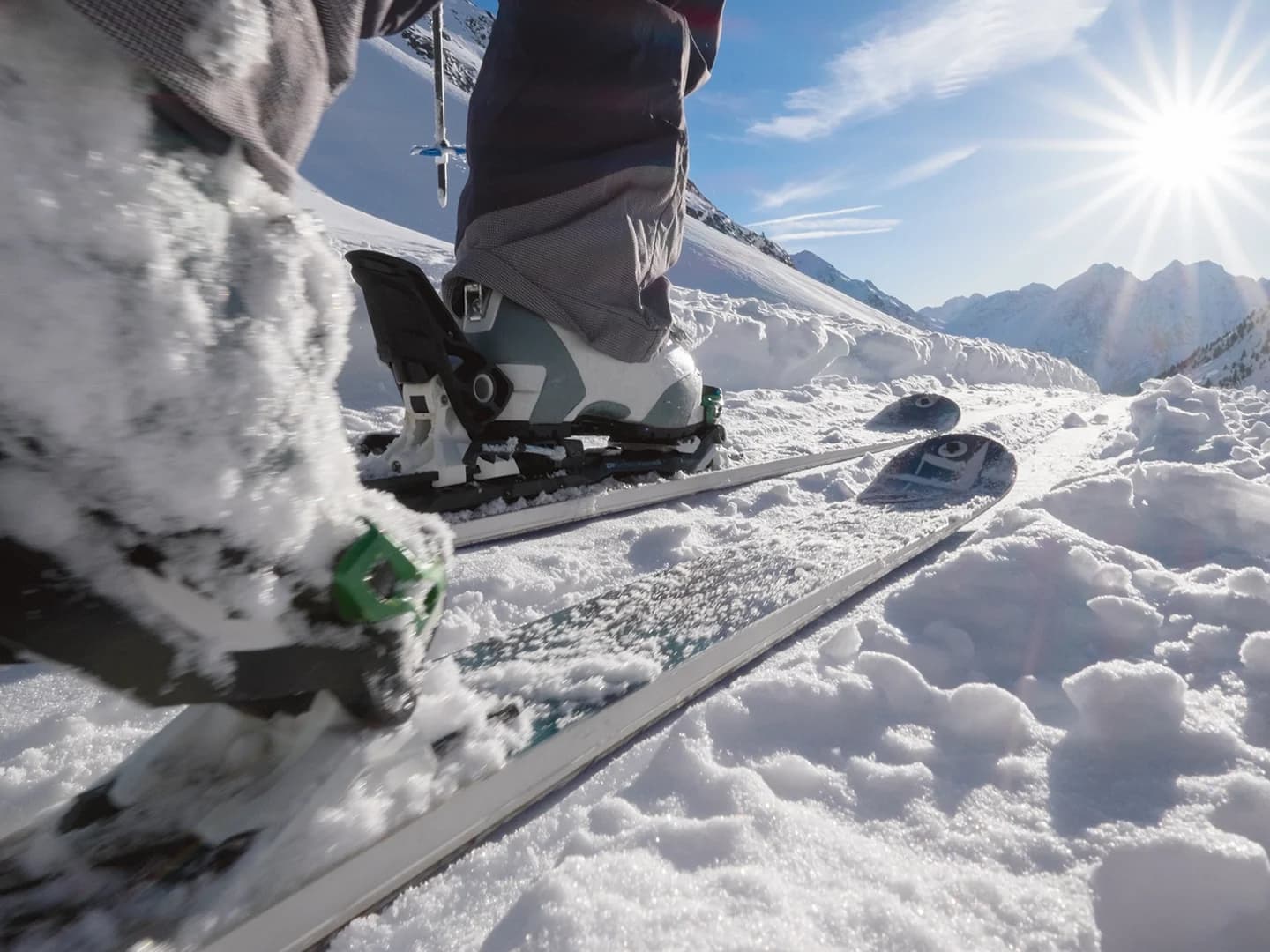 Nahaufnahme der in Skier eingeklickten Skischuhe einer Person, die durch frischen Schnee gleitet und die Essenz eines perfekten Winterurlaubs an einem sonnigen Berghang einfängt.