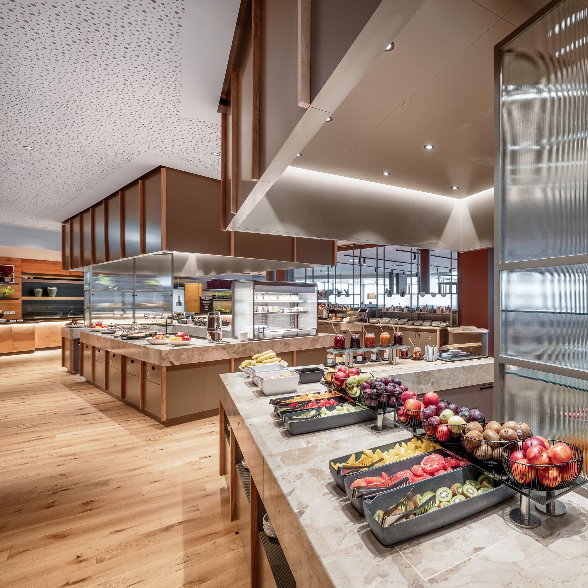 Ein modernes Buffet mit Marmortheken bietet eine Auswahl an frischem Obst und Frühstücksprodukten in einem offenen, hellen Essbereich mit Holzböden.