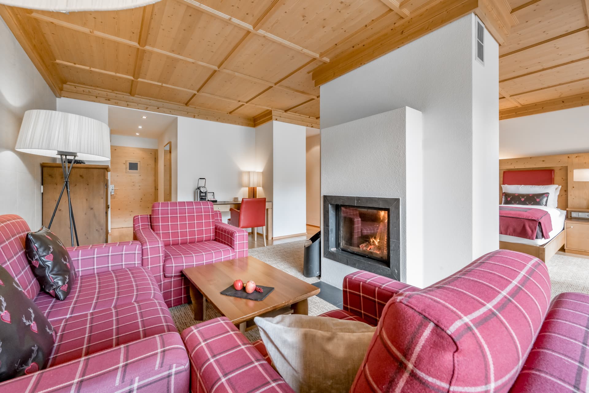 Уютная гостиная с розовыми клетчатыми креслами, деревянным журнальным столиком и камином; в соседней комнате стоит кровать.