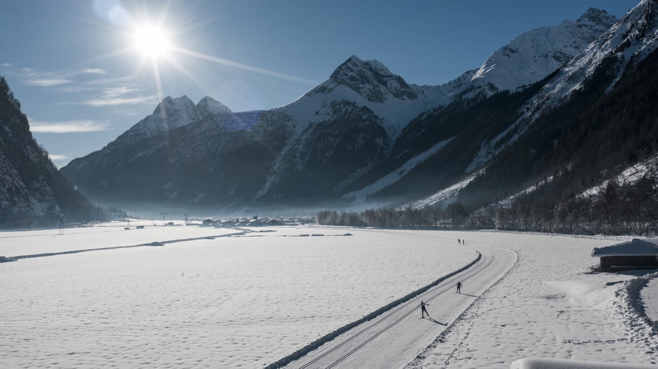 Langlaufspur im verschneiten Ötztal, mit ein paar Langläufern und Berggipfeln im Hintergrund bei strahlendem Sonnenschein. Ötztal Tourismus, Federico Modica - XC-ski.de Natur Panoramaaufnahme