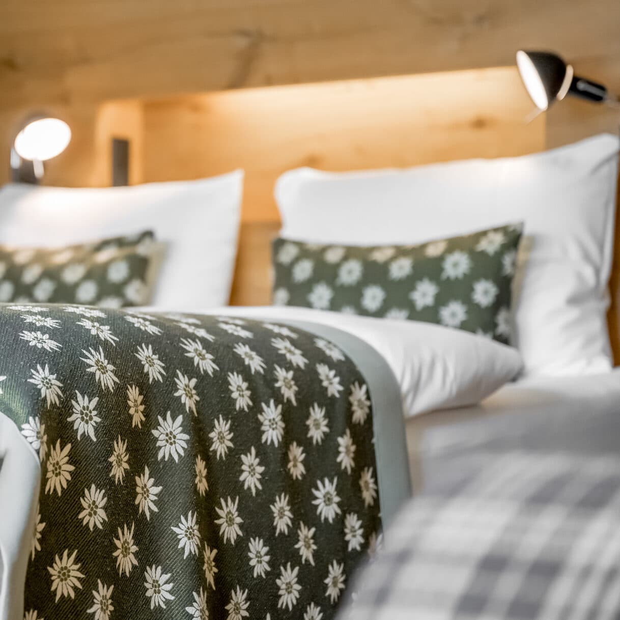 Nahaufnahme eines ordentlich gemachten Bettes mit weißen Kissen, grünen Blumenkissen und einer passenden grünen Blumendecke in einem gut beleuchteten Raum.