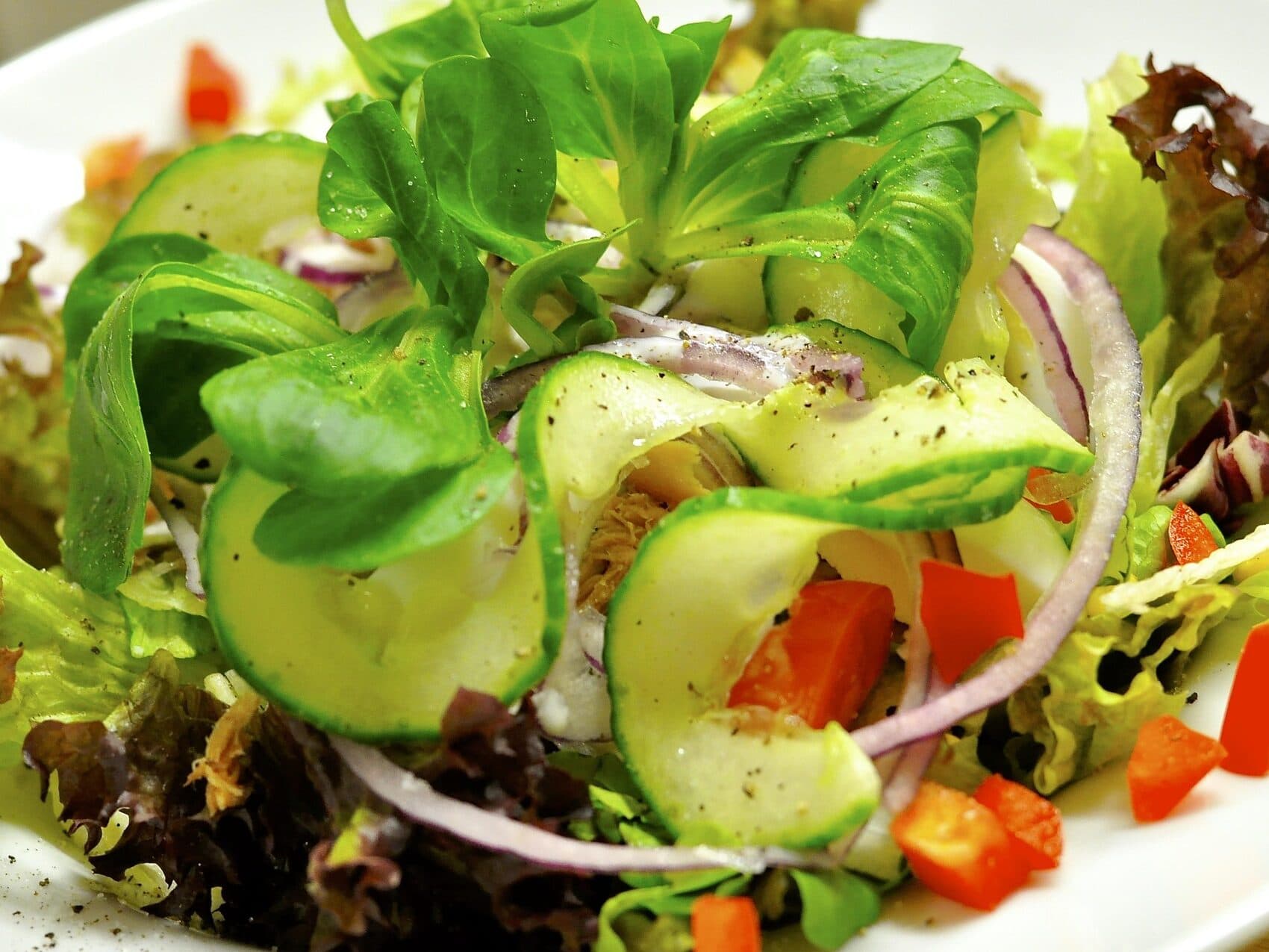 Un'insalata fresca con zucchine a fette, peperoni rossi, cipolle rosse, verdure a foglia e una spolverata di pepe nero.