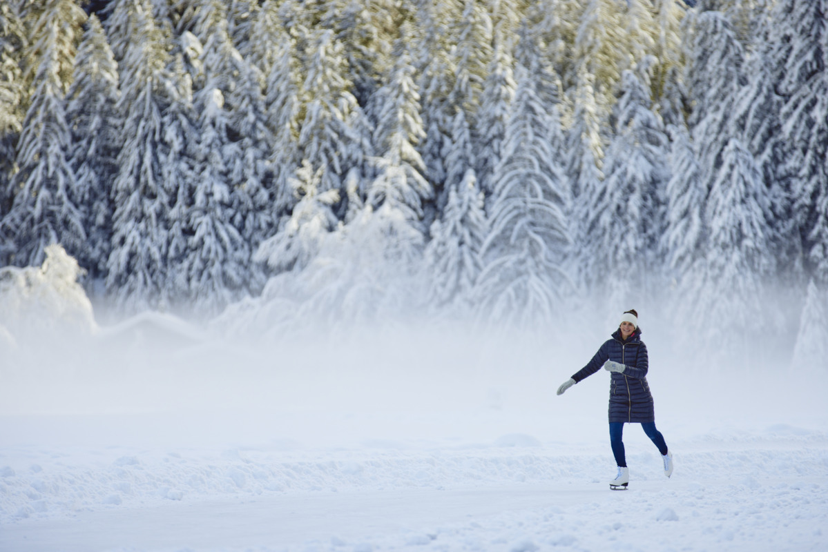 A person ice skating outdoors on a snowy path surrounded by snow-covered trees and mist in a winter landscape.