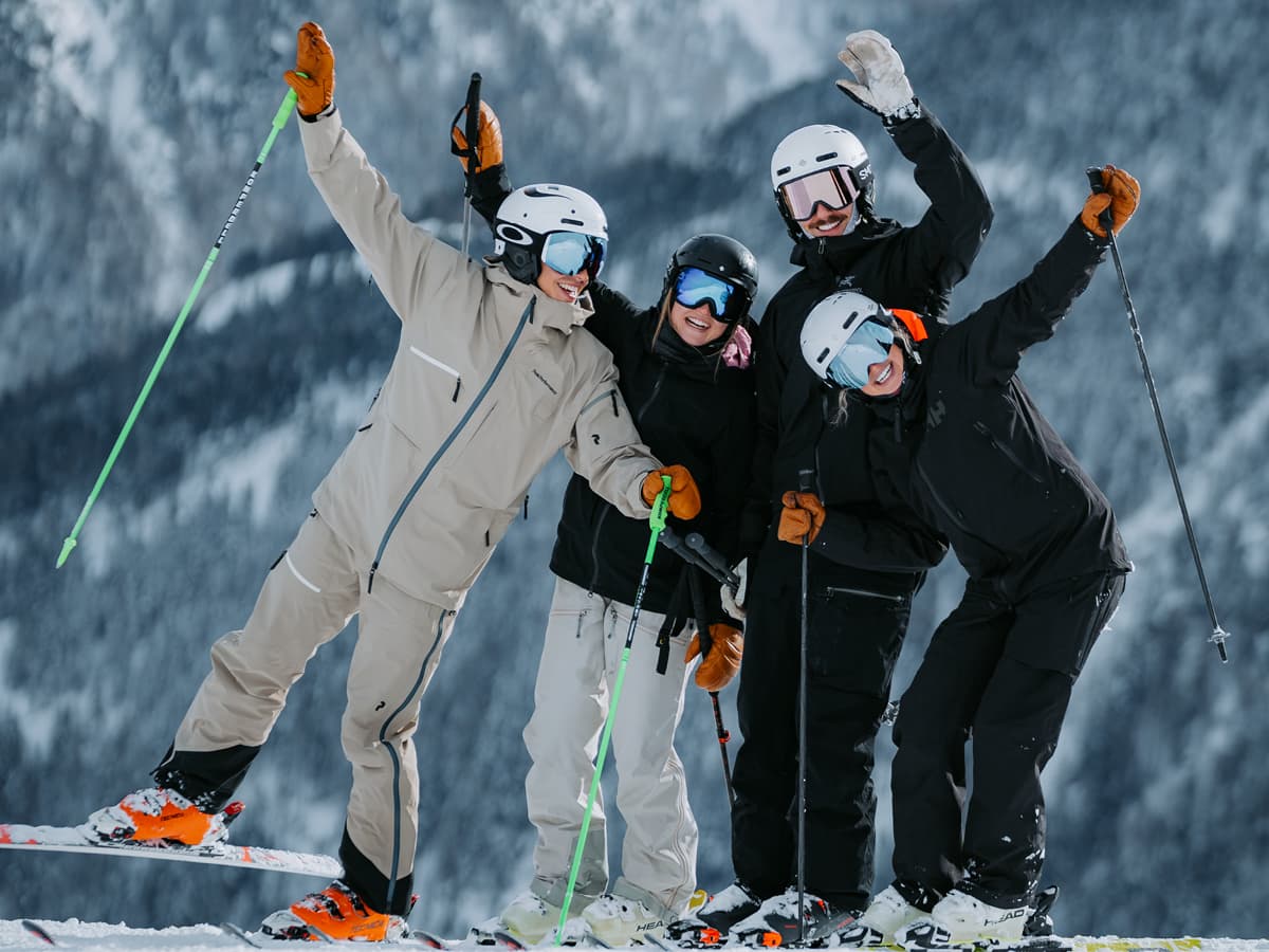 Vier Personen in Skikleidung stehen auf einem verschneiten Hang, lächeln und posieren für ein Gruppenfoto, während sie ihre Skistöcke vor einer Bergkulisse in die Höhe strecken – eine belebende Abwechslung zu den Besprechungen und die perfekte Gelegenheit, außerhalb des Büros den Zusammenhalt zu stärken.