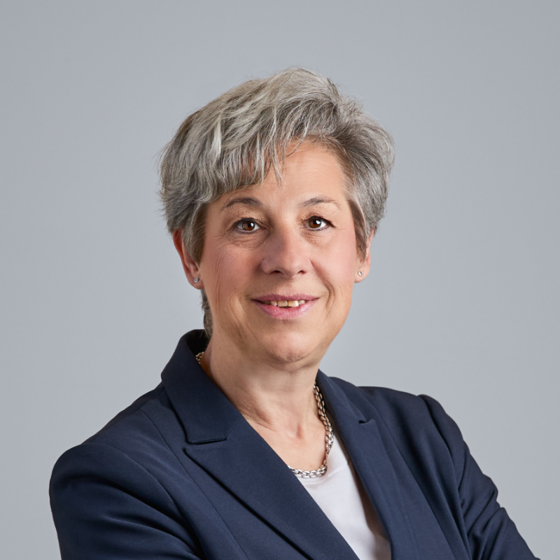 Nahaufnahme einer Frau mittleren Alters mit kurzen grauen Haaren, die einen dunkelblauen Blazer trägt.