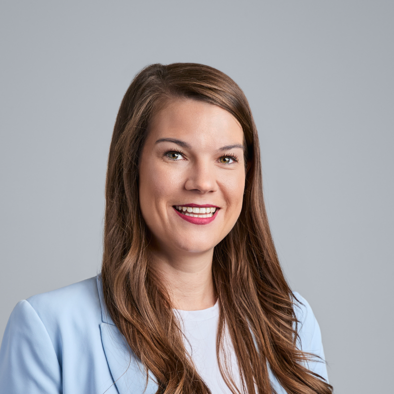 Headshot of a smiling woman with long brown hair wearing a light blue blazer.